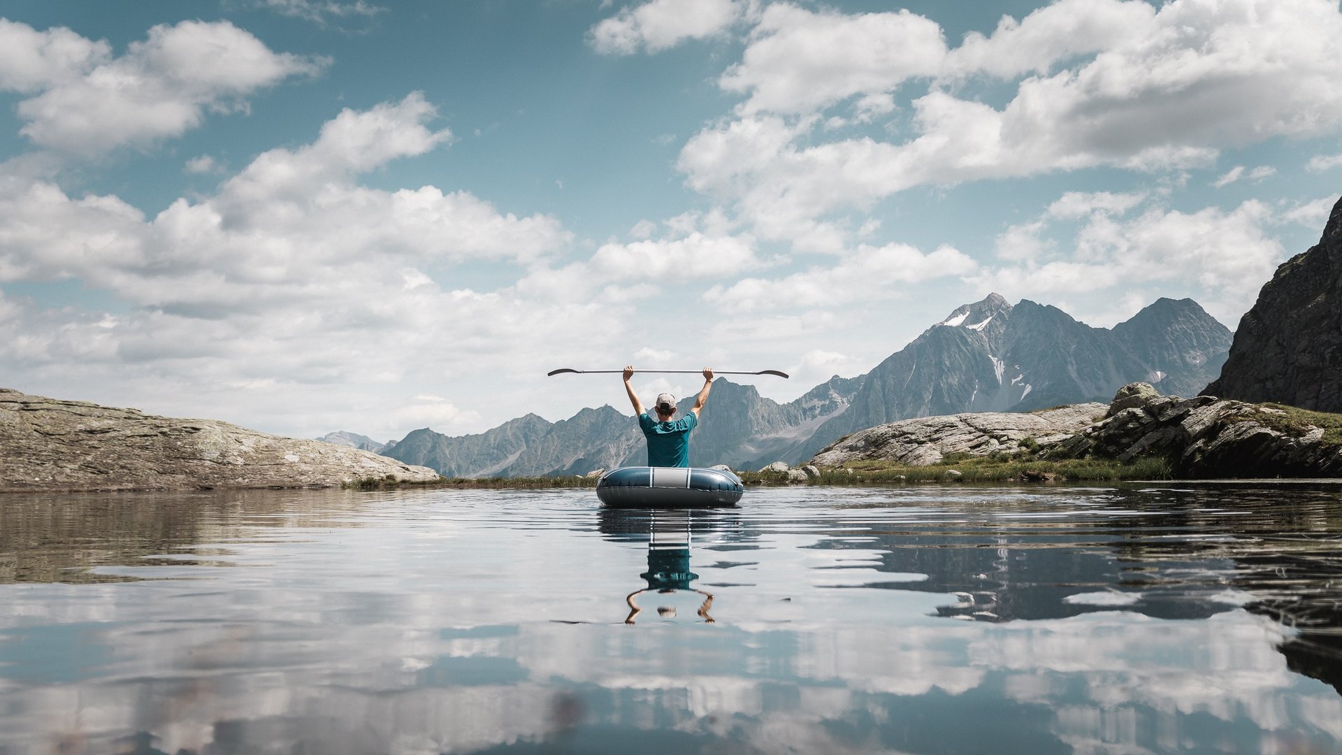 Deine Ferienwohnung in Neustift ✓ Person in Schlauchboot hebt Paddel in Bergsee unter bewölktem Himmel