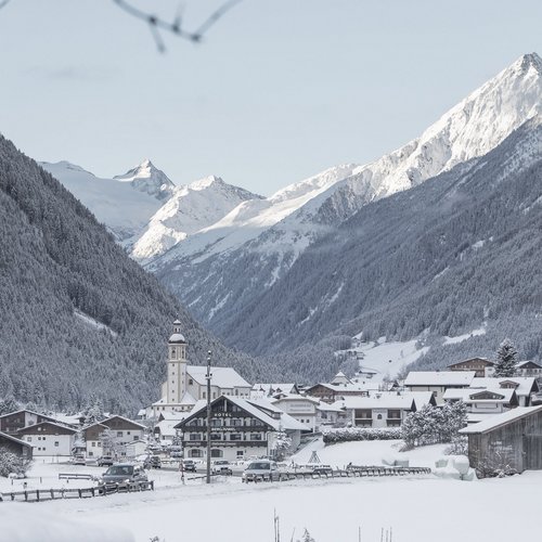 Deine Ferienwohnung in Neustift ✓ Verschneites Bergdorf mit Kirchturm und schneebedeckten Alpen im Hintergrund