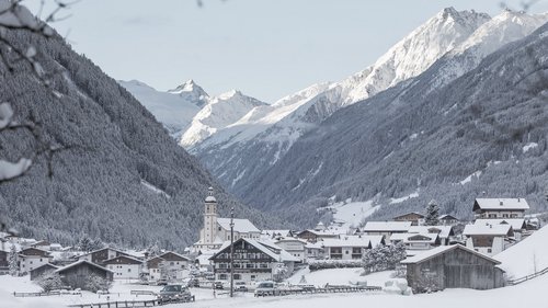 Deine Ferienwohnung in Neustift ✓ Verschneites Bergdorf mit Kirchturm und schneebedeckten Alpen im Hintergrund