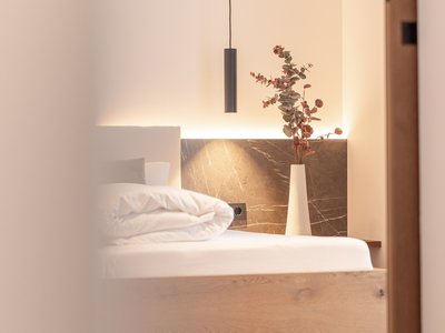 Deine Ferienwohnung in Neustift ✓ Moderner Schlafzimmerbereich mit Holzbett, Vase mit Zweigen und Pendelleuchte