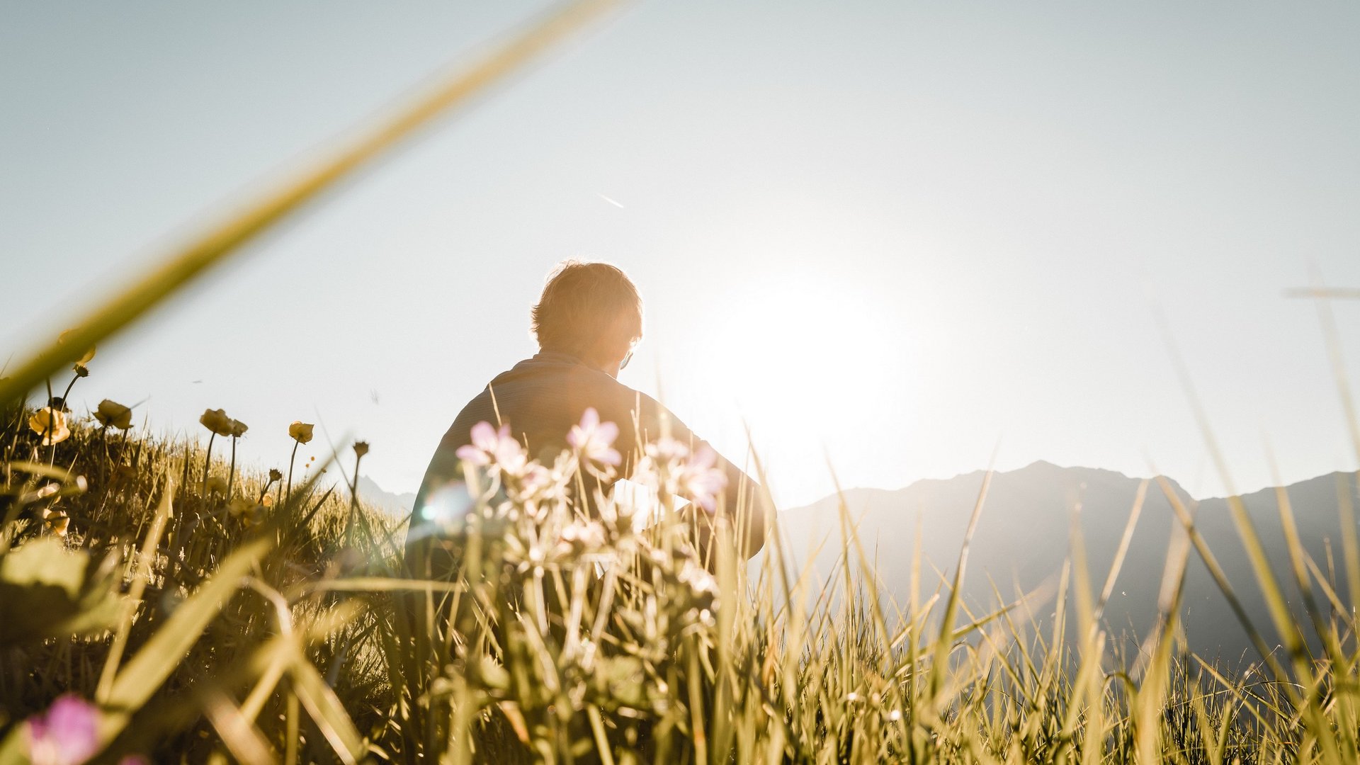 Deine Ferienwohnung in Neustift ✓ Person sitzt im Gras bei Sonnenaufgang in den Bergen