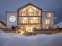 Deine Ferienwohnung in Neustift ✓ Beleuchtetes Apartmenthaus im Winter mit Schnee und Schnee fällt abends