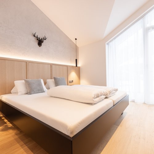 Deine Ferienwohnung in Neustift ✓ Modernes Schlafzimmer mit großem Bett, Holzboden und großem Fenster