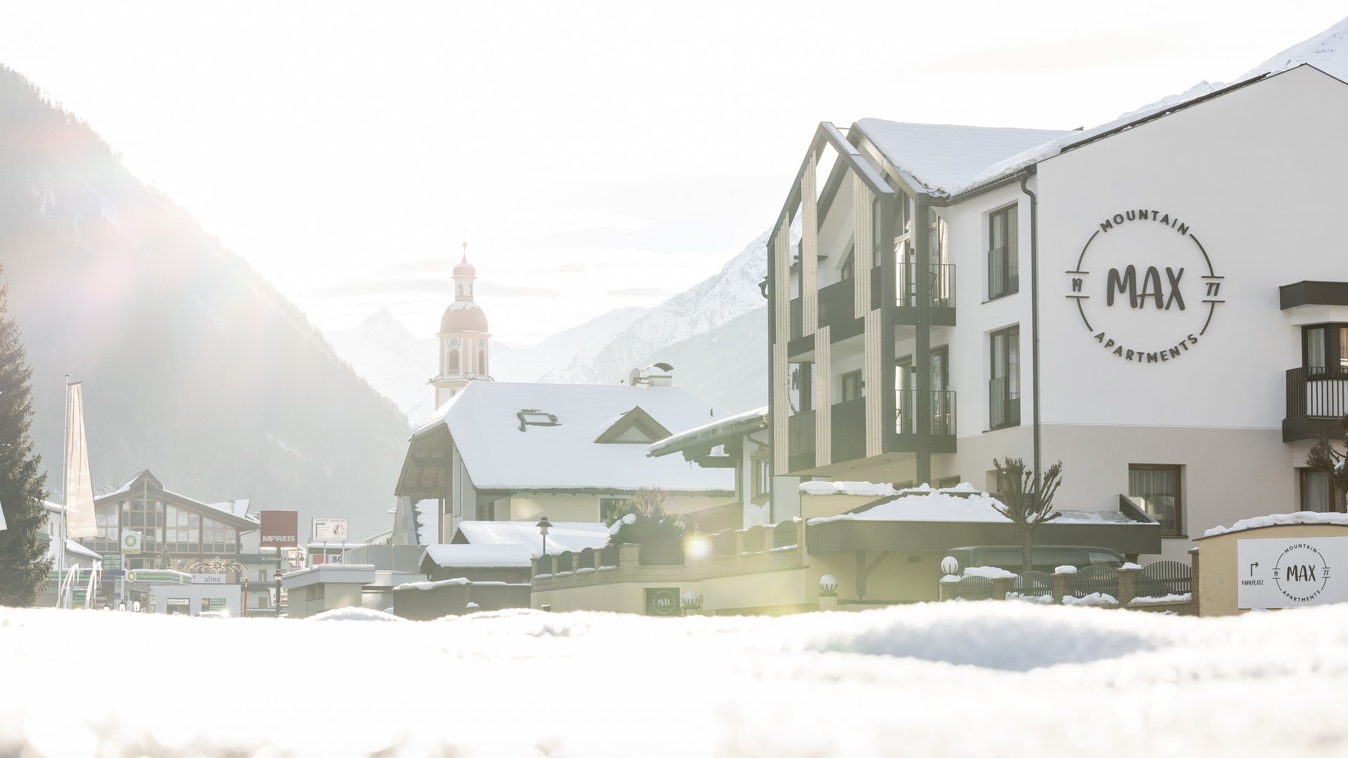 Deine Ferienwohnung in Neustift ✓ Verschneites Bergdorf mit Apartments und Kirche im Hintergrund
