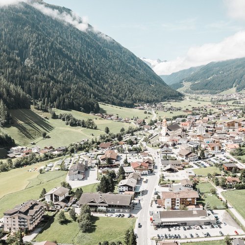 Deine Ferienwohnung in Neustift ✓ Blick auf ein Dorf in einem grünen Tal zwischen bewaldeten Bergen