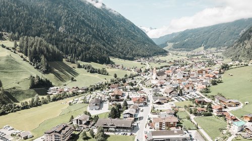 Deine Ferienwohnung in Neustift ✓ Blick auf ein Dorf in einem grünen Tal zwischen bewaldeten Bergen